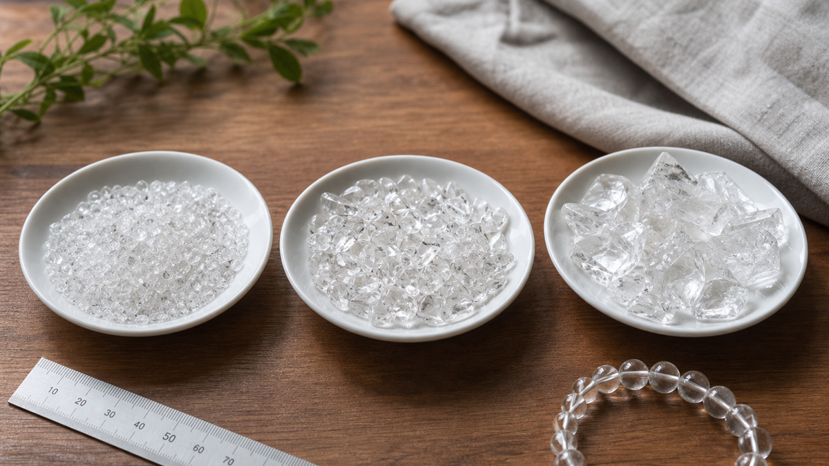 木の机に小粒、中粒、大粒の水晶さざれ石を入れた白い皿を並べ、横に水晶ブレスレットと定規を置いた様子